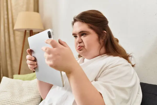 Confident young woman with Down syndrome enjoys a moment of leisure while using her tablet at home. — Stock Photo