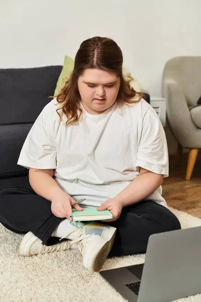 A young woman with Down syndrome sits on the floor at home, focused on her laptop. — Stock Photo