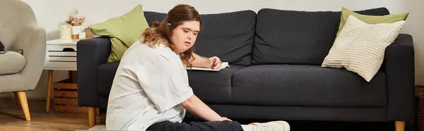 A young woman with Down syndrome sits at home, focused on a creative task in cozy decor. — Stock Photo