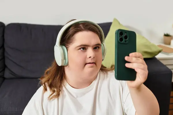 A young woman with Down syndrome sits at home, comfortably on a call with headphones. — Stock Photo