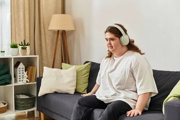 A young woman with Down syndrome sits comfortably at home, immersed in music and relaxation. — Stock Photo