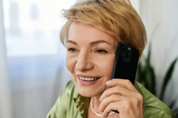 Senior woman with short blonde hair enjoys a warm conversation on her mobile phone while seated. — Stock Photo