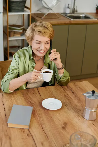 Donna anziana con un sorriso radioso gode di caffè mentre parla al telefono in una cucina accogliente. — Foto stock