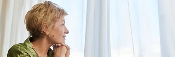 Beautiful mature woman enjoys a quiet moment while looking out a sunlit window in the afternoon. — Stock Photo