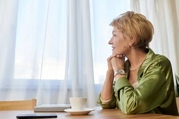 Mature woman sits thoughtfully by a window, admiring the gentle light in a serene setting. — Stock Photo