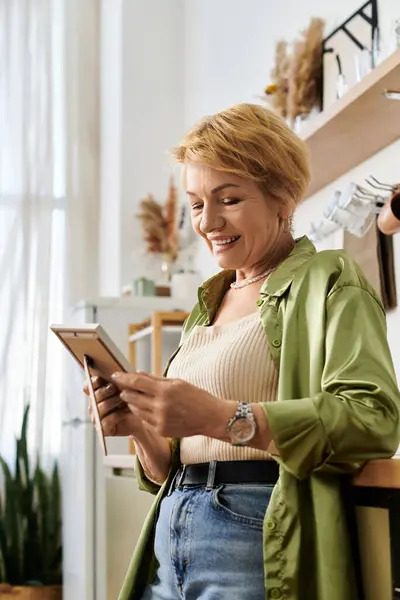 Mujer mayor sonriente se involucra con su tableta en una acogedora habitación llena de plantas. - foto de stock
