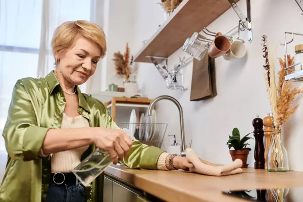 Пожилая женщина убирает свою кухню с заботой и радостью, в окружении тепла и света. — стоковое фото