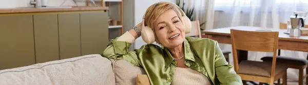 A beautiful senior woman enjoys a relaxing moment at home, smiling while wearing cozy headphones. — Stock Photo