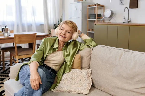 A beautiful senior woman relaxes in her cozy living room, enjoying music with a bright smile. — Stock Photo