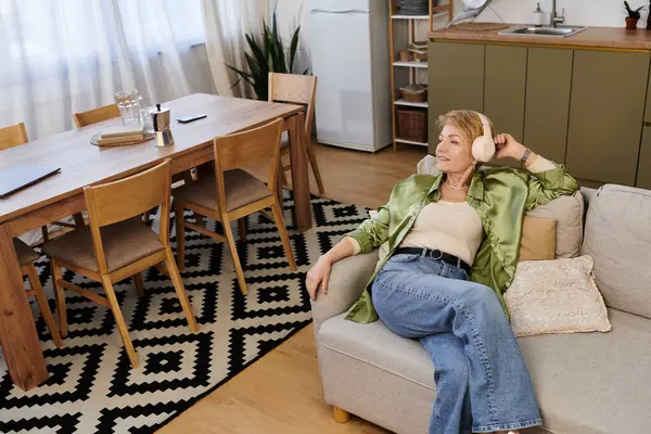 Mature woman enjoys a serene moment in a stylish living space, surrounded by warmth and comfort. — Stock Photo