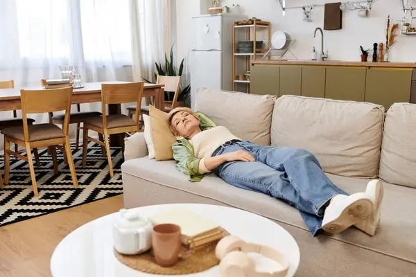 A lovely senior woman relaxes on a cozy couch in her warm afternoon living room. — Stock Photo
