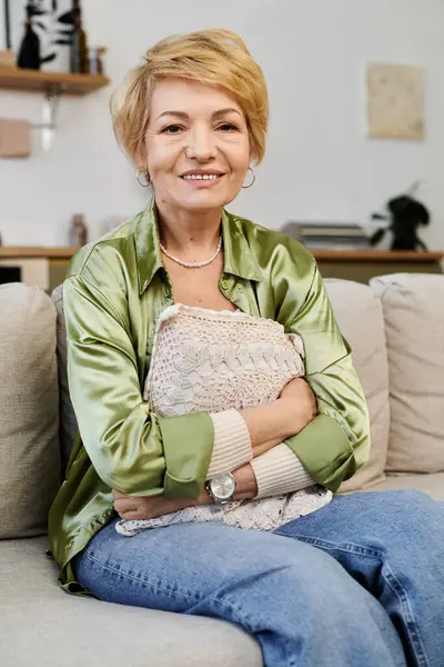 Eine schöne Seniorin entspannt sich auf der Couch mit einer weichen Decke und lächelt in ihrem gemütlichen Wohnzimmer. — Stockfoto