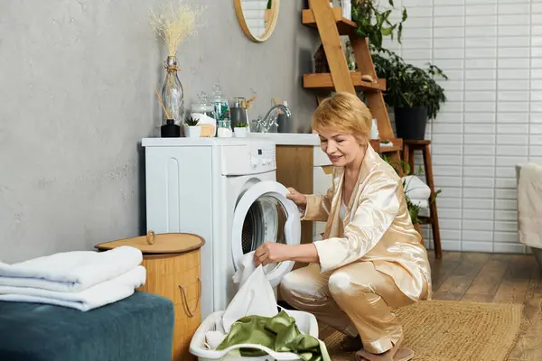 Eine fröhliche Seniorin im weichen Pyjama faltet Wäsche in einem schicken, pflanzengefüllten Wohnraum. — Stockfoto