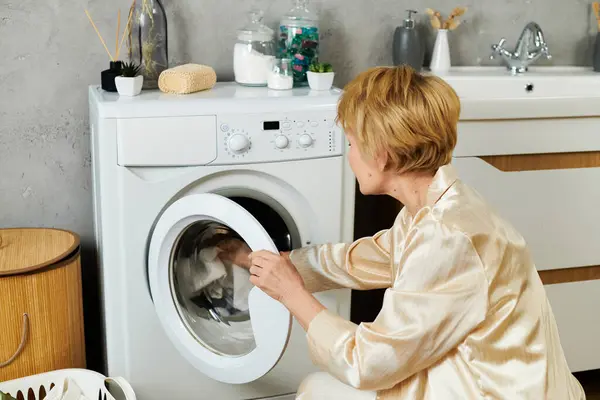 Eine hübsche Seniorin wäscht in ihrem schicken Haus mit einer Waschmaschine. — Stockfoto