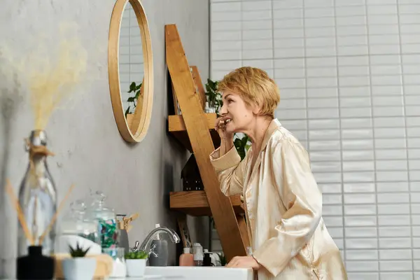 Bella donna anziana in un abito elegante sorride al suo riflesso, preparandosi per il giorno a venire. — Foto stock