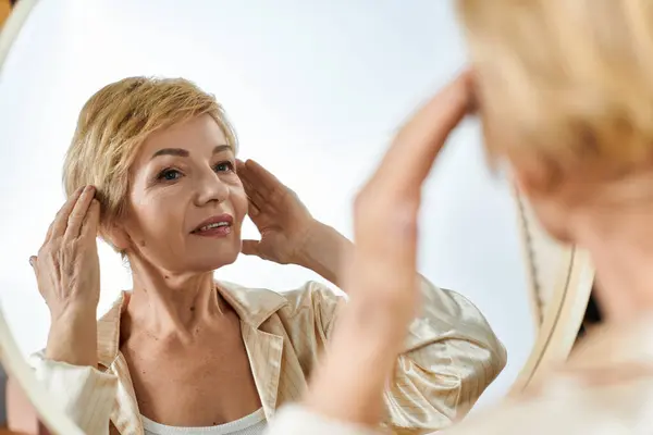 Bella donna anziana guarda in uno specchio, regolando la sua acconciatura con grazia e fiducia. — Foto stock