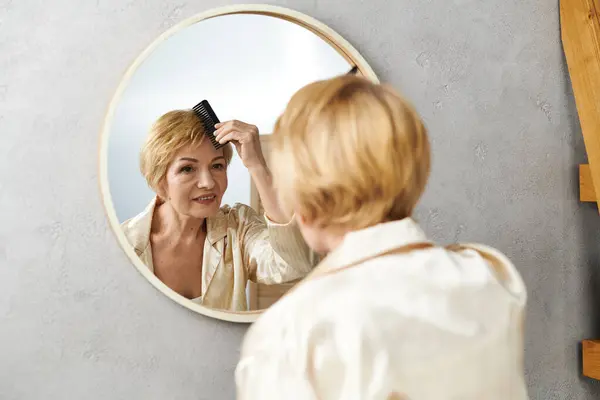 Una donna anziana sorride mentre si spoglia i capelli in uno specchio in una mattina tranquilla. — Foto stock
