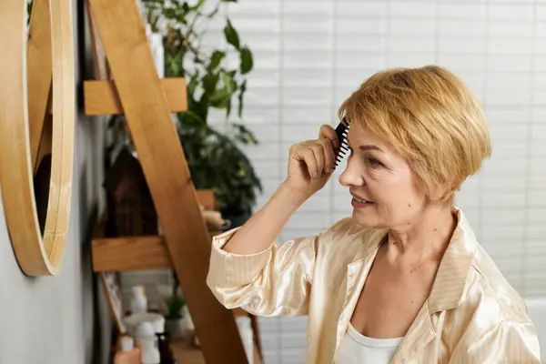 Una bella donna anziana stili i suoi capelli corti ammirando il suo riflesso in uno spazio moderno. — Foto stock