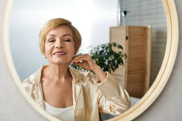 Donna anziana con un bel sorriso si tocca il collo mentre si guarda in uno specchio rotondo all'interno. — Foto stock