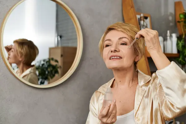 Reife Frau genießt ihre Hautpflege-Routine, während sie ihr Spiegelbild in einem stilvollen Spiegel betrachtet. — Stockfoto