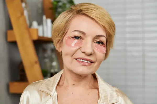 Красива старша жінка наносить зволожуючі плями під очима, світячи з радістю і впевненістю. — стокове фото