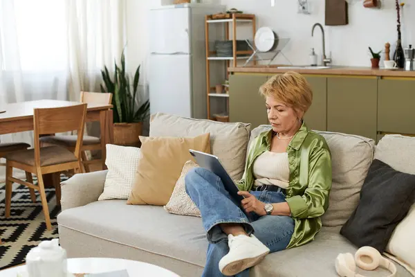 A joyful senior woman reads on her tablet while relaxing in her cozy living room. — Stock Photo