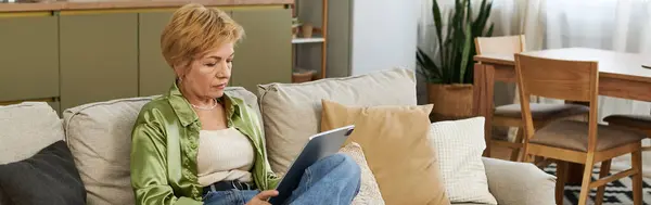 Una mujer madura con el pelo corto y rubio se involucra con su tableta en un entorno tranquilo en casa. - foto de stock