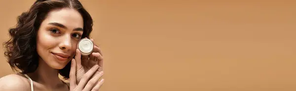 Hübsche junge Frau unterstreicht ihre Hautpflege-Routine mit einem Produkt in gemütlicher Studioatmosphäre, Banner — Stockfoto