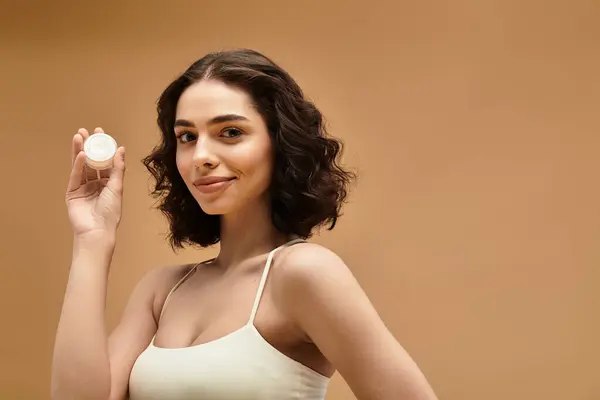 Pretty young woman showcases her beauty and skincare routine while smiling and holding a product. — Stock Photo