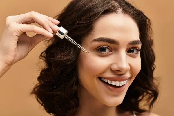 This young woman highlights her skincare routine using a serum while smiling confidently. — Stock Photo