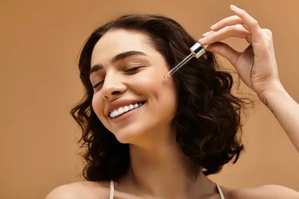 Una giovane donna applica gioiosamente il siero per la cura della pelle in uno studio luminoso, mostrando la sua routine di bellezza. — Foto stock