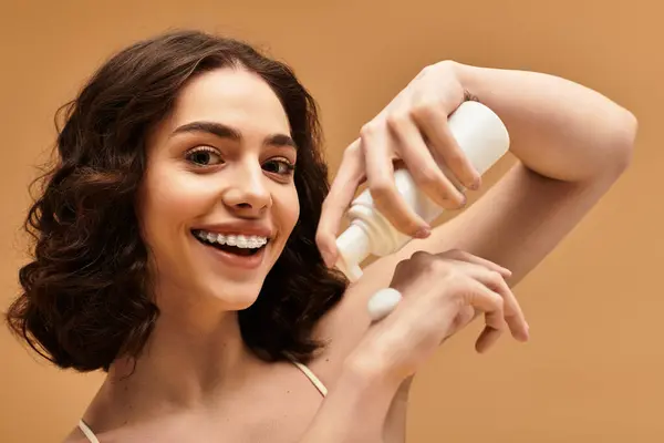 A young woman with braces happily demonstrates her beauty skincare routine in a warm studio. — Stock Photo