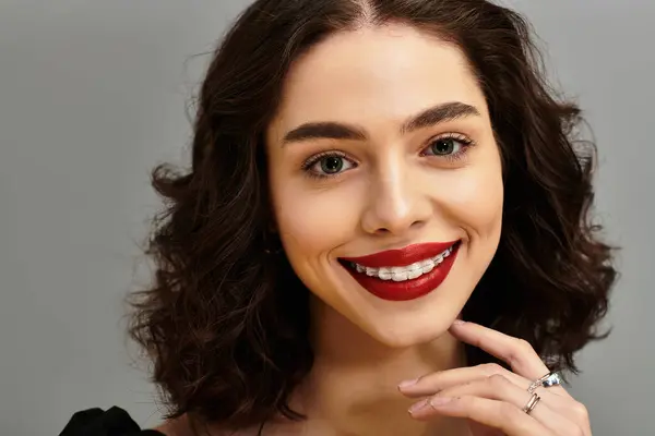 A captivating young woman with curly hair smiles confidently, highlighting her red lips and braces. — Stock Photo