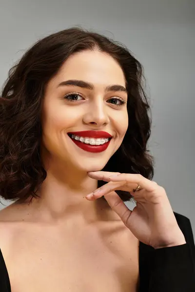 Una hermosa joven muestra su sonrisa radiante, completa con frenillos y labios rojos audaces. - foto de stock