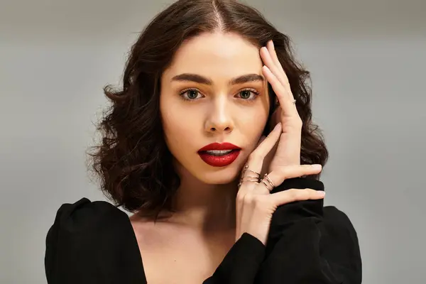 Una giovane donna mette in mostra le sue belle bretelle e labbra rosse su uno sfondo grigio morbido. — Foto stock