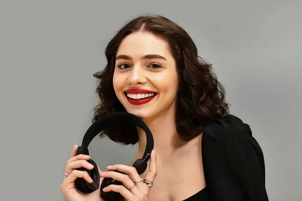 A beautiful young woman with striking red lips smiles brightly while holding headphones. — Stock Photo