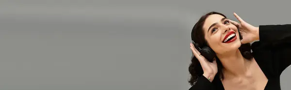 A stylish young woman with red lips smiles while listening to music in trendy headphones, banner — Stock Photo