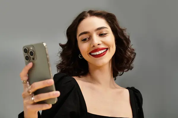 Smiling young woman with red lips and braces looks at her phone, radiating joy and confidence. — Stock Photo
