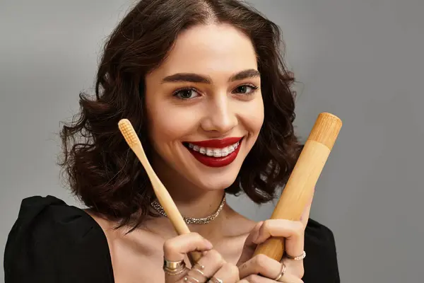 Uma jovem com lábios vermelhos mostra seus aparelhos e ferramentas dentárias contra um fundo cinza. — Fotografia de Stock