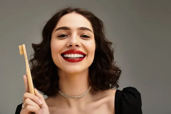 Uma jovem mostra seu lindo sorriso com lábios e aparelhos vermelhos, segurando uma escova de dentes. — Fotografia de Stock