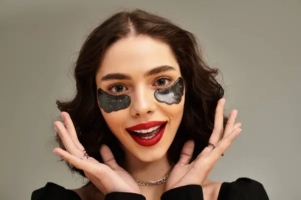 Brightly smiling young woman with red lips and braces poses confidently with under eye patches for moisturising skin — Stock Photo