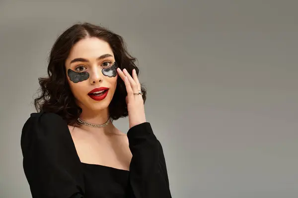 A beautiful young woman showcases her striking red lips and under eye patches, adding charm to her look. — Stock Photo
