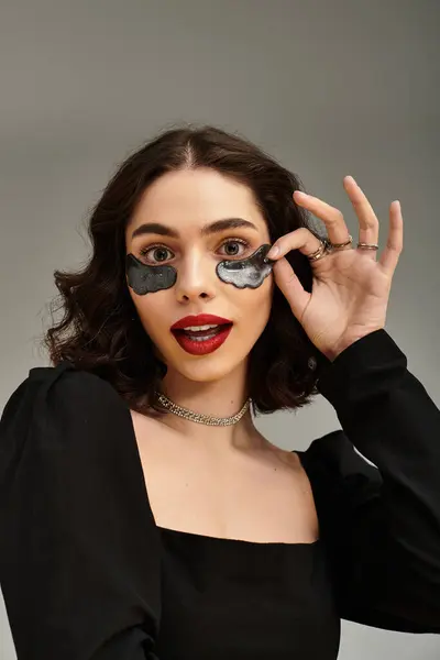 A young woman with braces playfully poses against a grey background, showcasing her under eye patches — Stock Photo