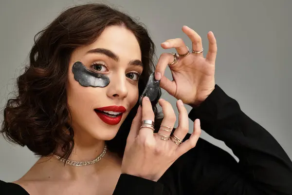 A charming young woman with braces poses playfully while applying under eye patches — Stock Photo