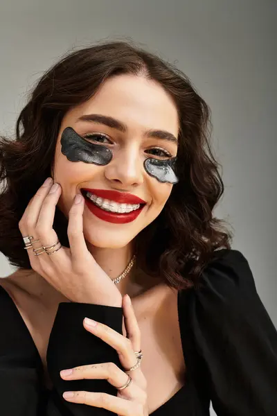 Bright smile lights up the grey backdrop as the young woman poses confidently, with under eye patches — Stock Photo
