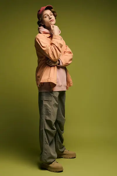 A young man stands confidently in a studio with a green backdrop, dressed in trendy casual wear. — Stock Photo