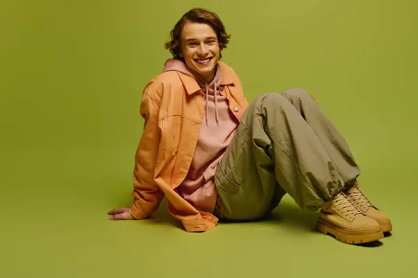 Vestido con estilo deportivo, un joven se sienta casualmente en el suelo, exudando confianza y encanto. - foto de stock
