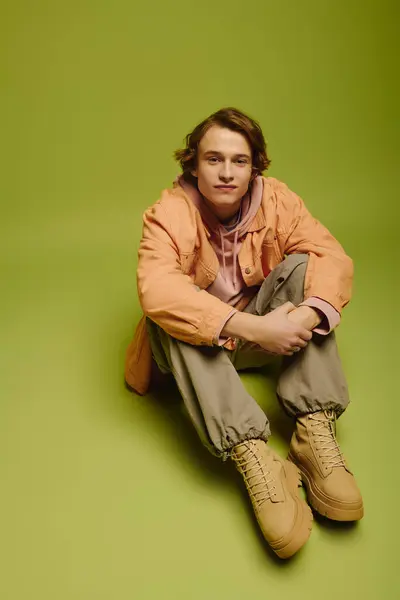 A young man in trendy clothes poses casually against a vibrant green background. — Stock Photo