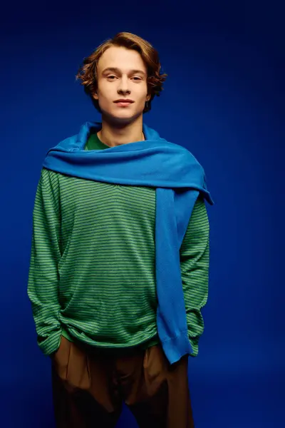 A stylish young man in modern attire confidently poses against a striking blue backdrop. — Stock Photo
