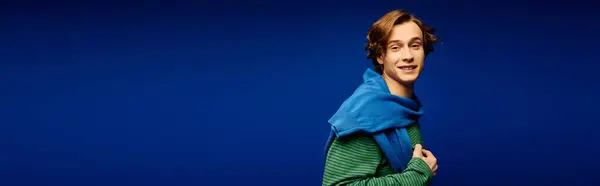 A stylish young man poses confidently in trendy attire against a bold blue background. — Stock Photo